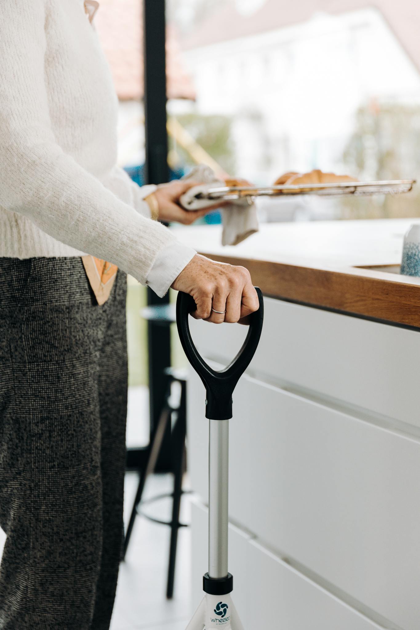 Senior adult holding a mobility aid while preparing food in a modern kitchen.