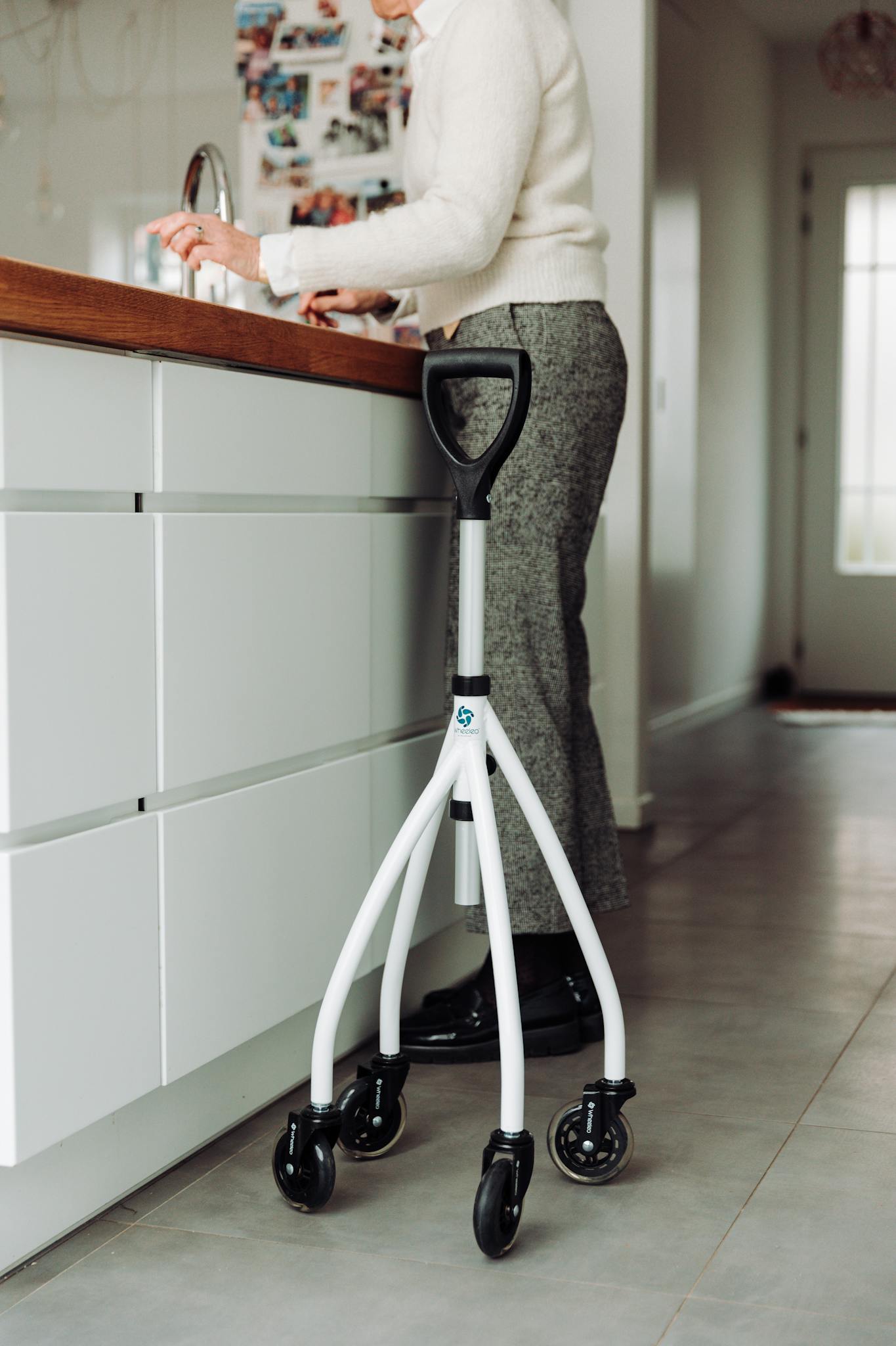 Senior adult using a rollator for support while in a modern kitchen setting.